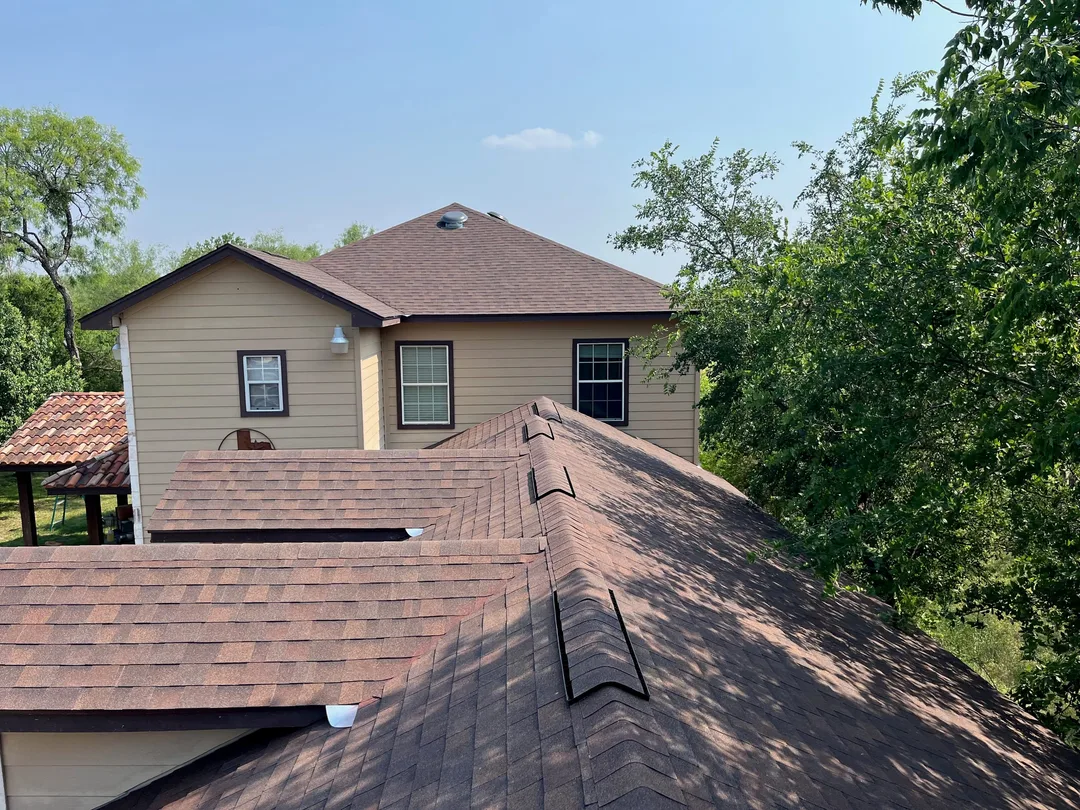 A brown shingle roof and the upper floor of a house seen from above, with trees beyond
