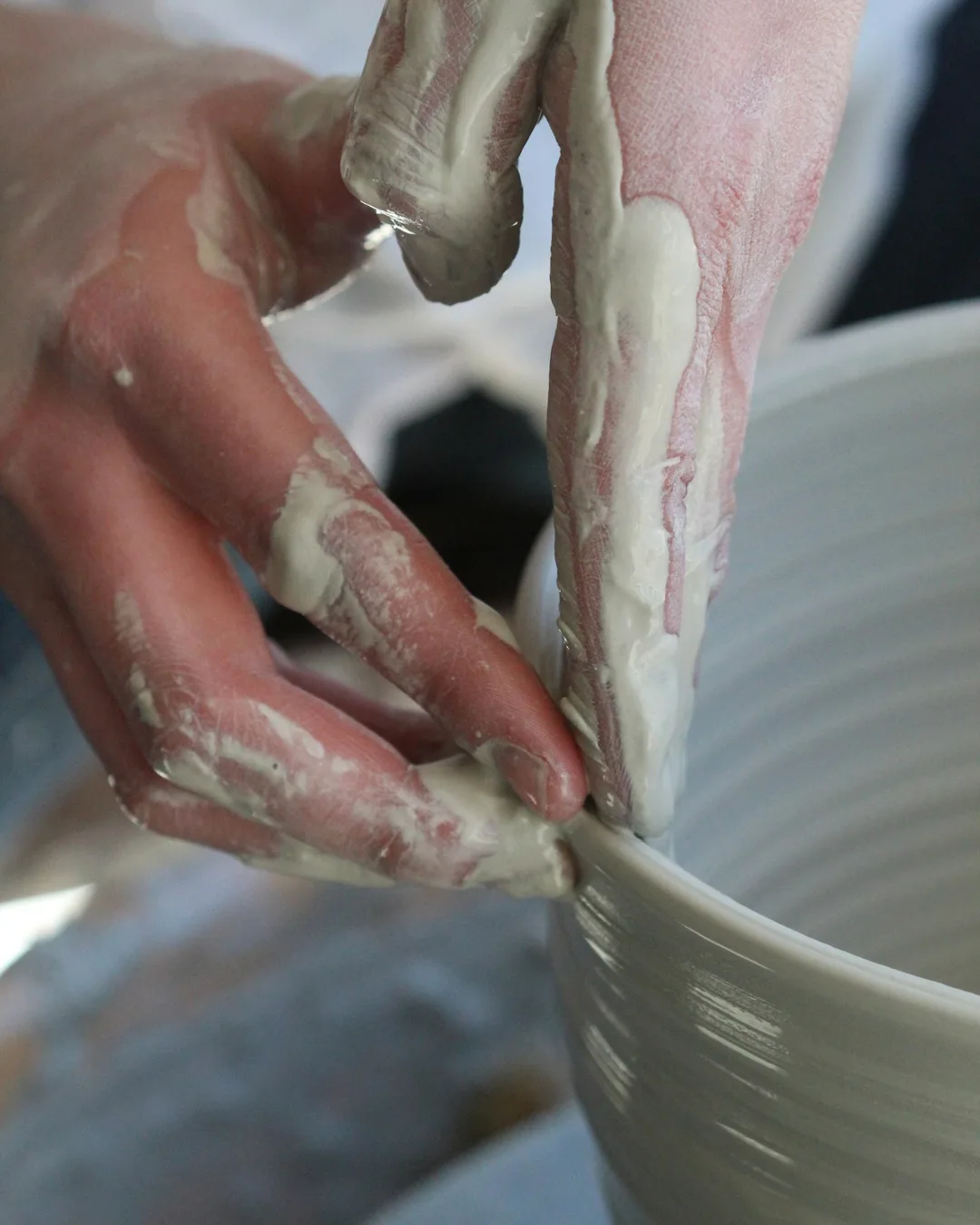 Clay-covered hands shaping a bowl rim on the wheel