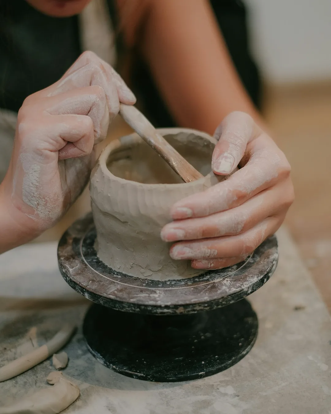 Hands smoothing a small clay pot on a banding wheel