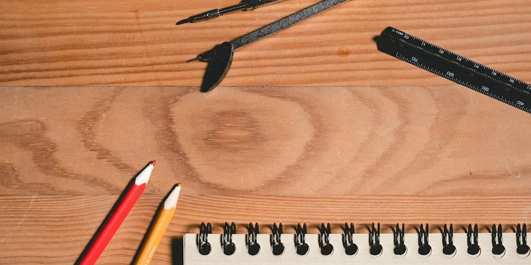 A blank sketchbook, pencils and a compass on a wooden desk