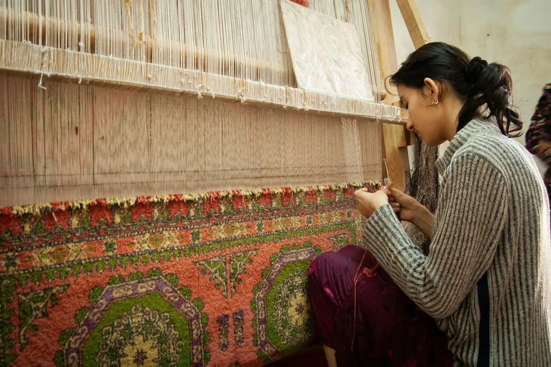 A weaver knotting a rug at an upright loom