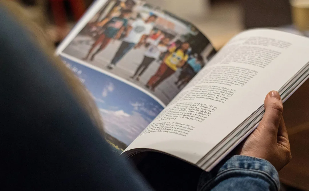 A reader holding open a magazine with photographs of people walking