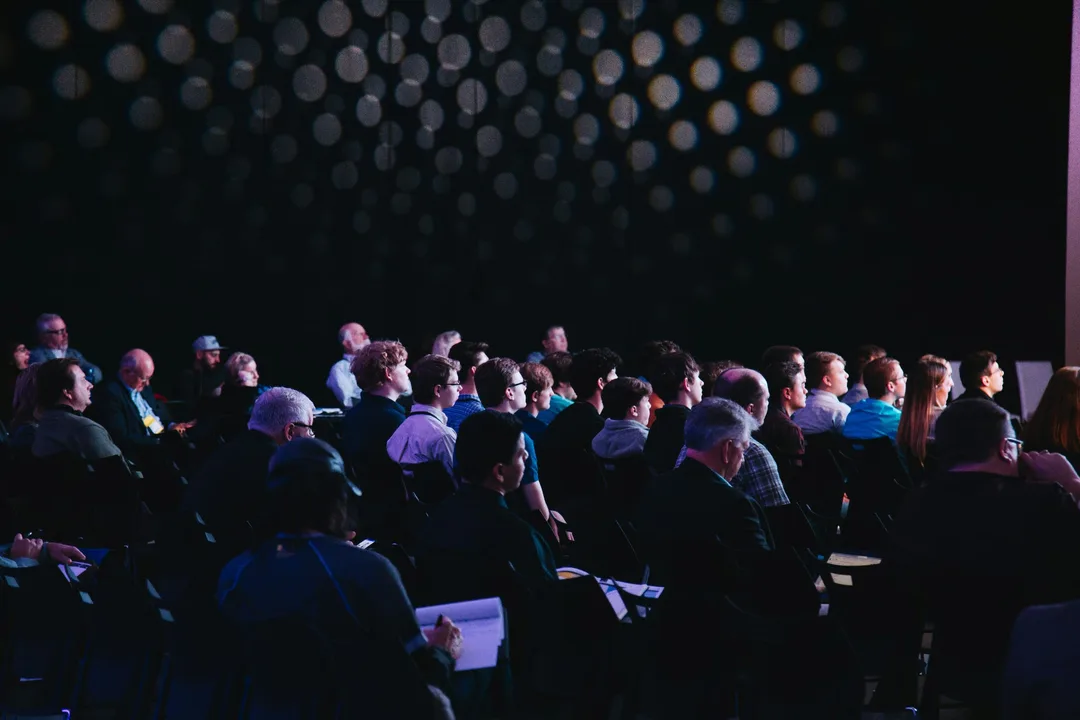 Rows of people seen from behind, watching a talk in a dark hall