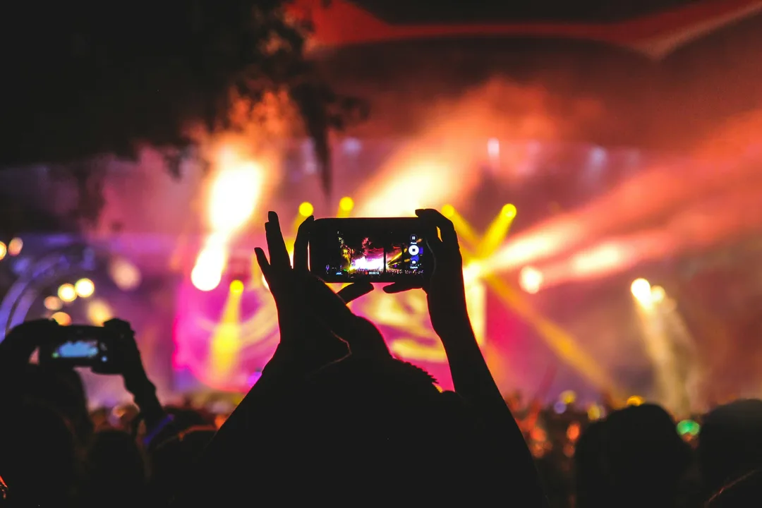 A hand holding up a phone to film a stage lit in pink and yellow