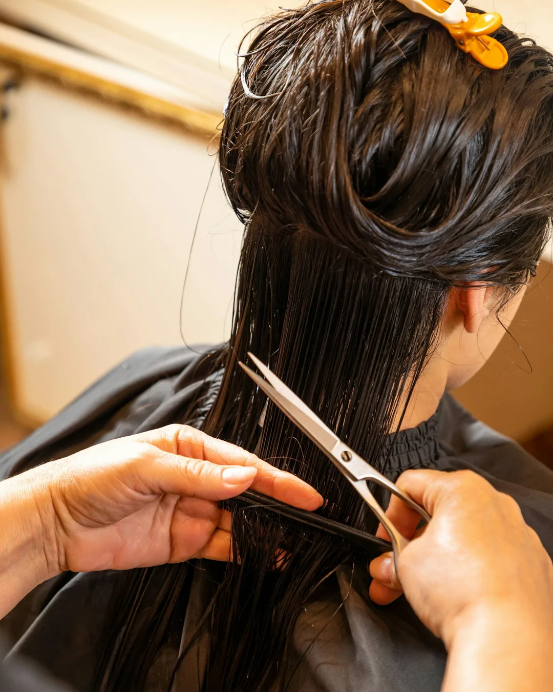 A stylist cutting long wet hair with scissors and a comb