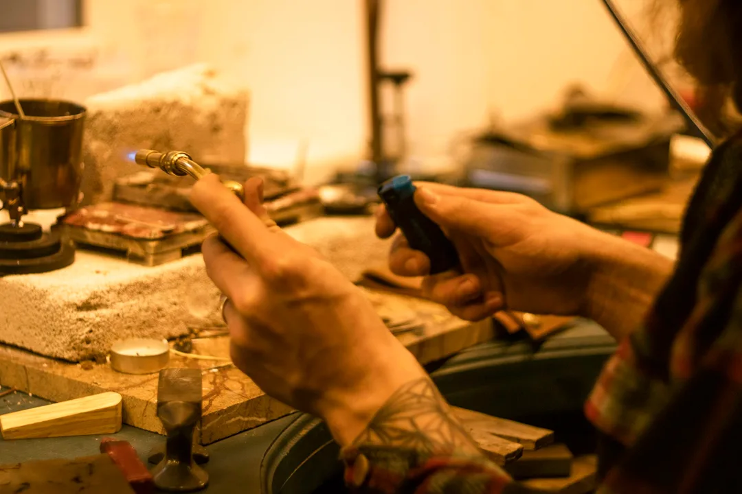 A jeweler soldering a piece at a bench with a small torch, in warm light