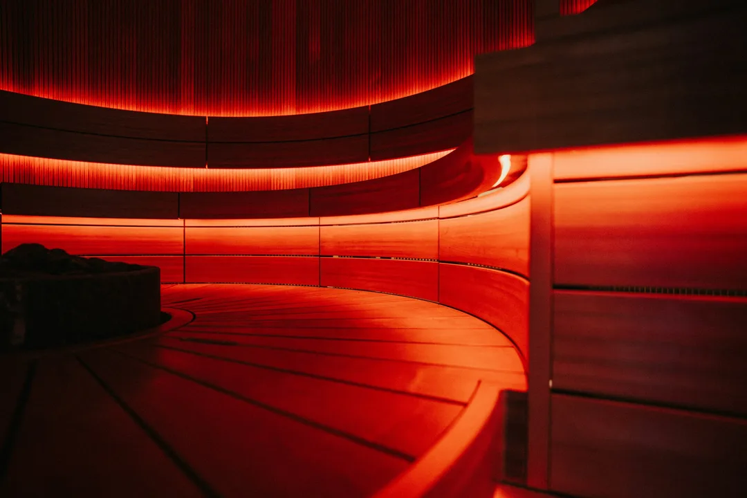 Curved wooden sauna benches lit in a warm red glow