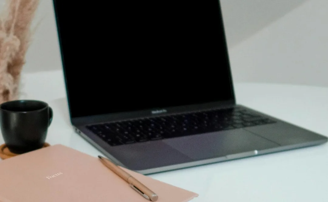 A tidy desk with a laptop, a notebook and a cup of coffee